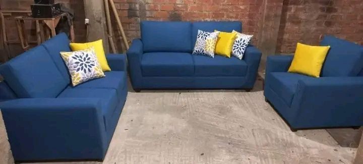 Conjunto de sofá azul con almohadones amarillos y estampados sobre un suelo de hormigón en un entorno rústico.