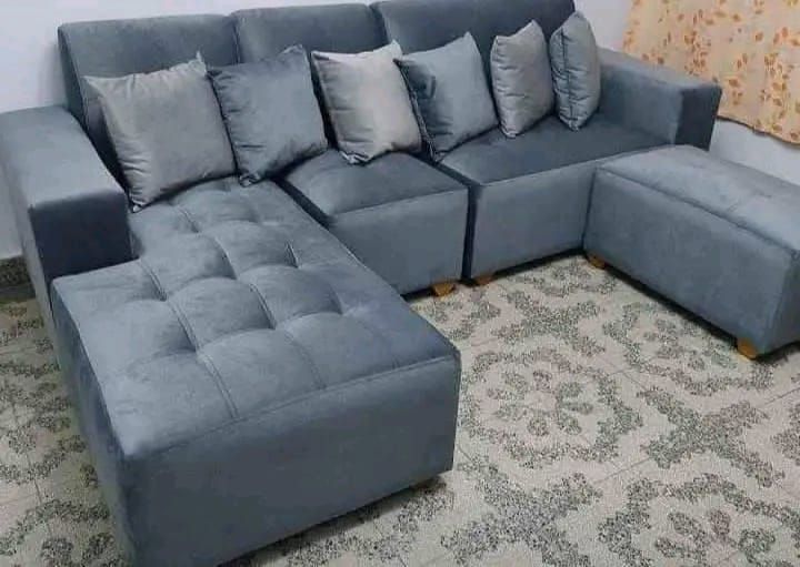 Sofá seccional gris con almohadas y otomana sobre alfombra estampada.