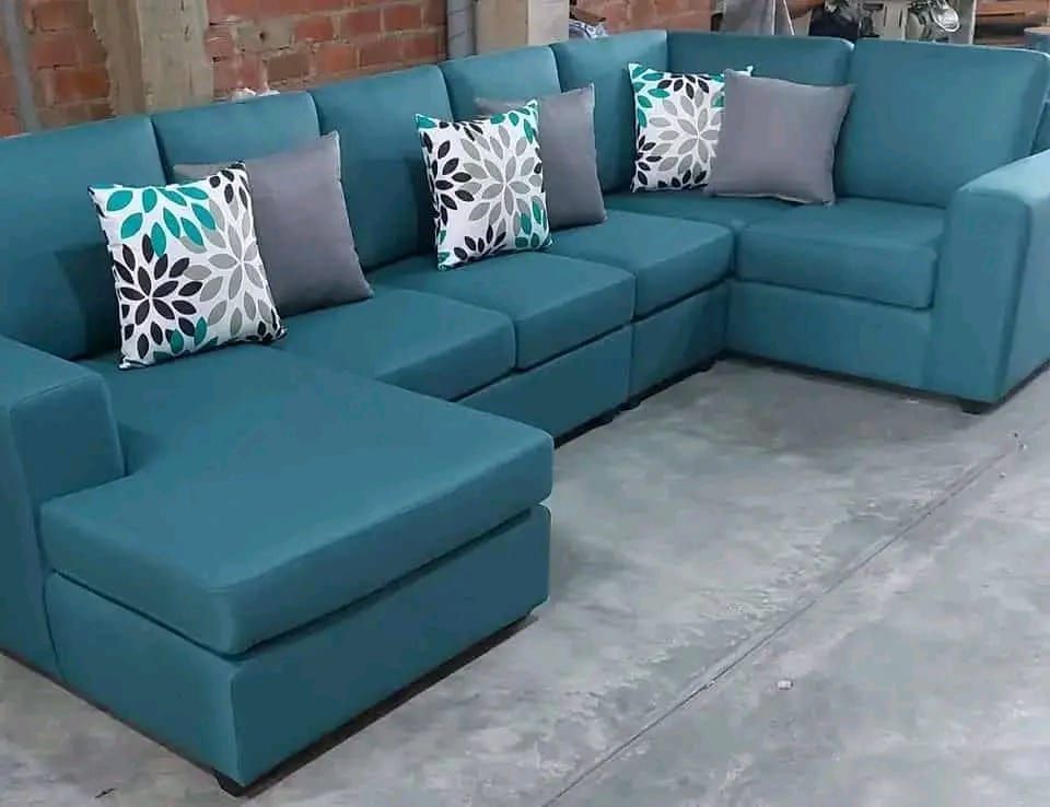 Sofá seccional color verde azulado con almohadones grises y florales en un ambiente interior.