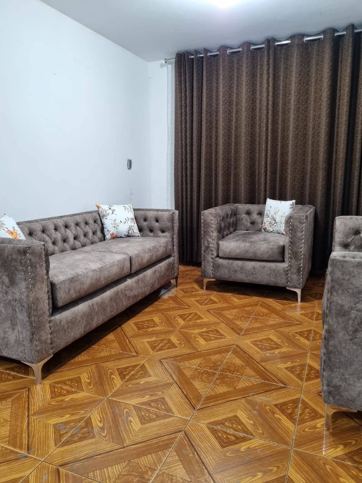 Sala de estar con sofá marrón, sillón y piso de madera estampado.
