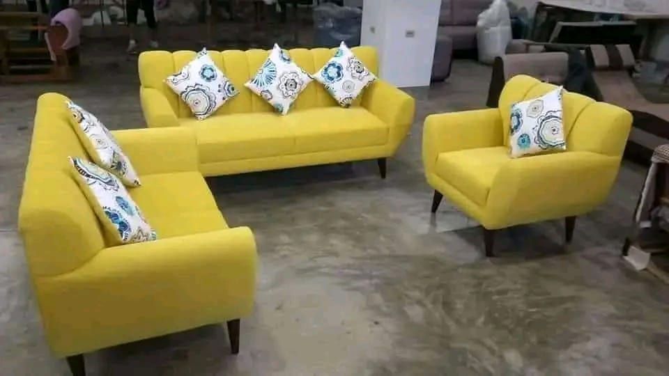 Conjunto de sofá tapizado en amarillo con almohadones sobre un piso de concreto.