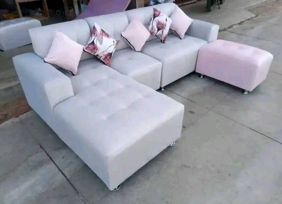 Sofá seccional gris claro con almohadones y otomana rosas.