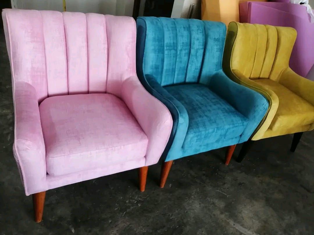 Tres sillones de terciopelo: rosa, verde azulado y amarillo, con patas de madera, dispuestos en fila.
