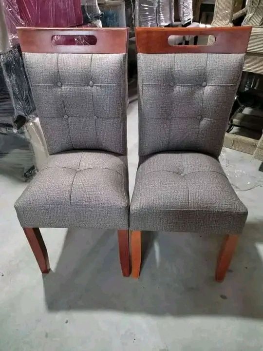 Dos sillas de comedor tapizadas en gris con marco de madera, una al lado de la otra.