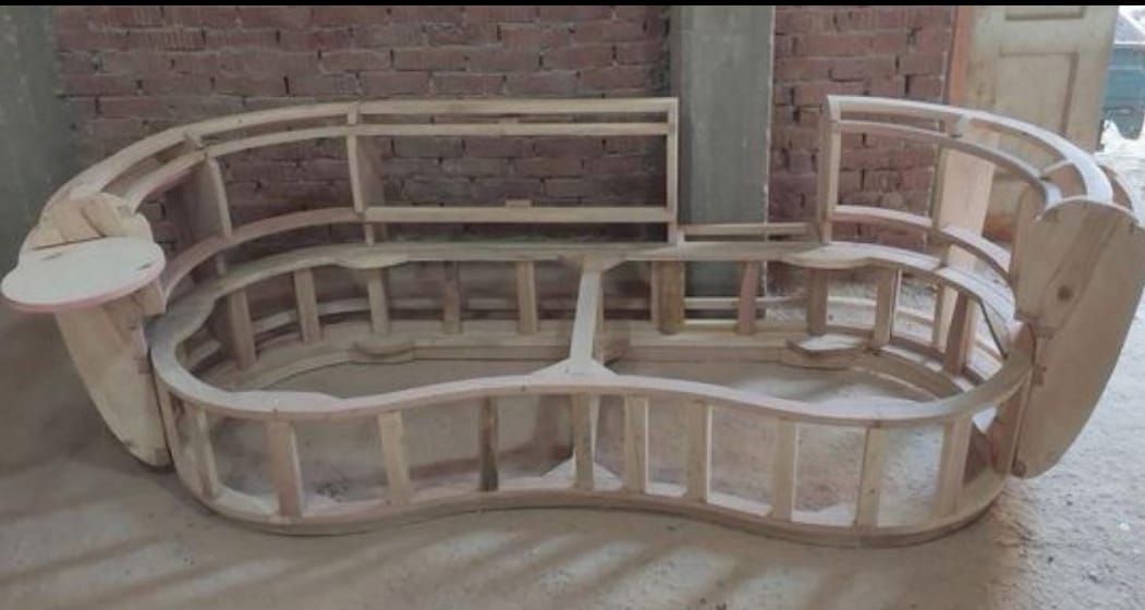 Estructura de sofá de madera en construcción; diseño curvo, color madera claro, sin terminar.