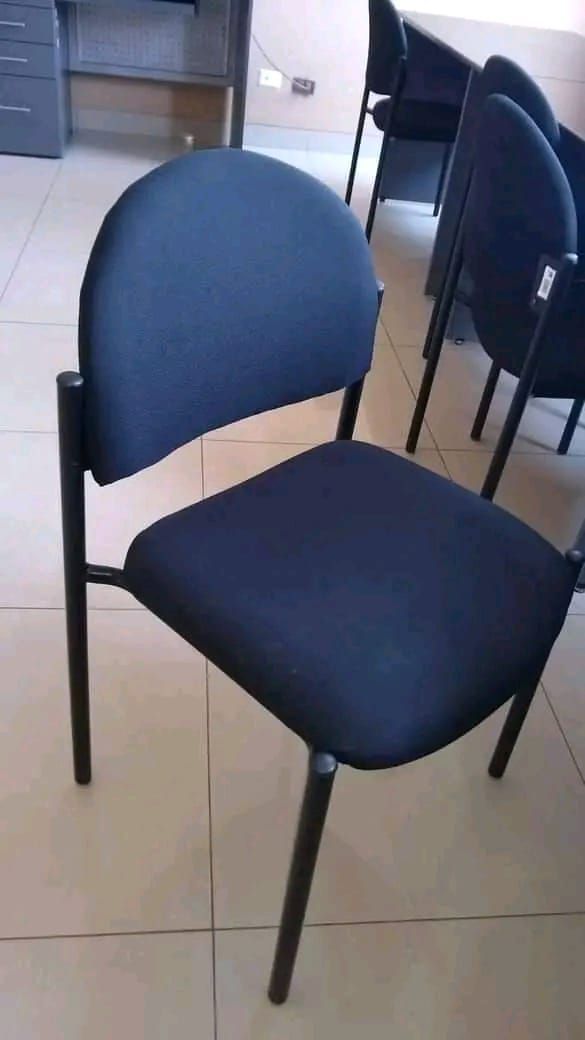 Silla tapizada en azul con patas negras en una habitación; otras sillas están al fondo.