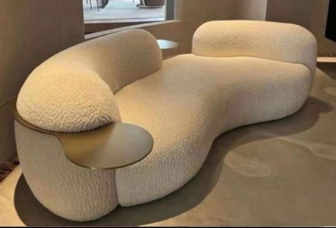 Sofá curvo de bouclé color crema con mesa auxiliar de latón. Diseño moderno para interiores.