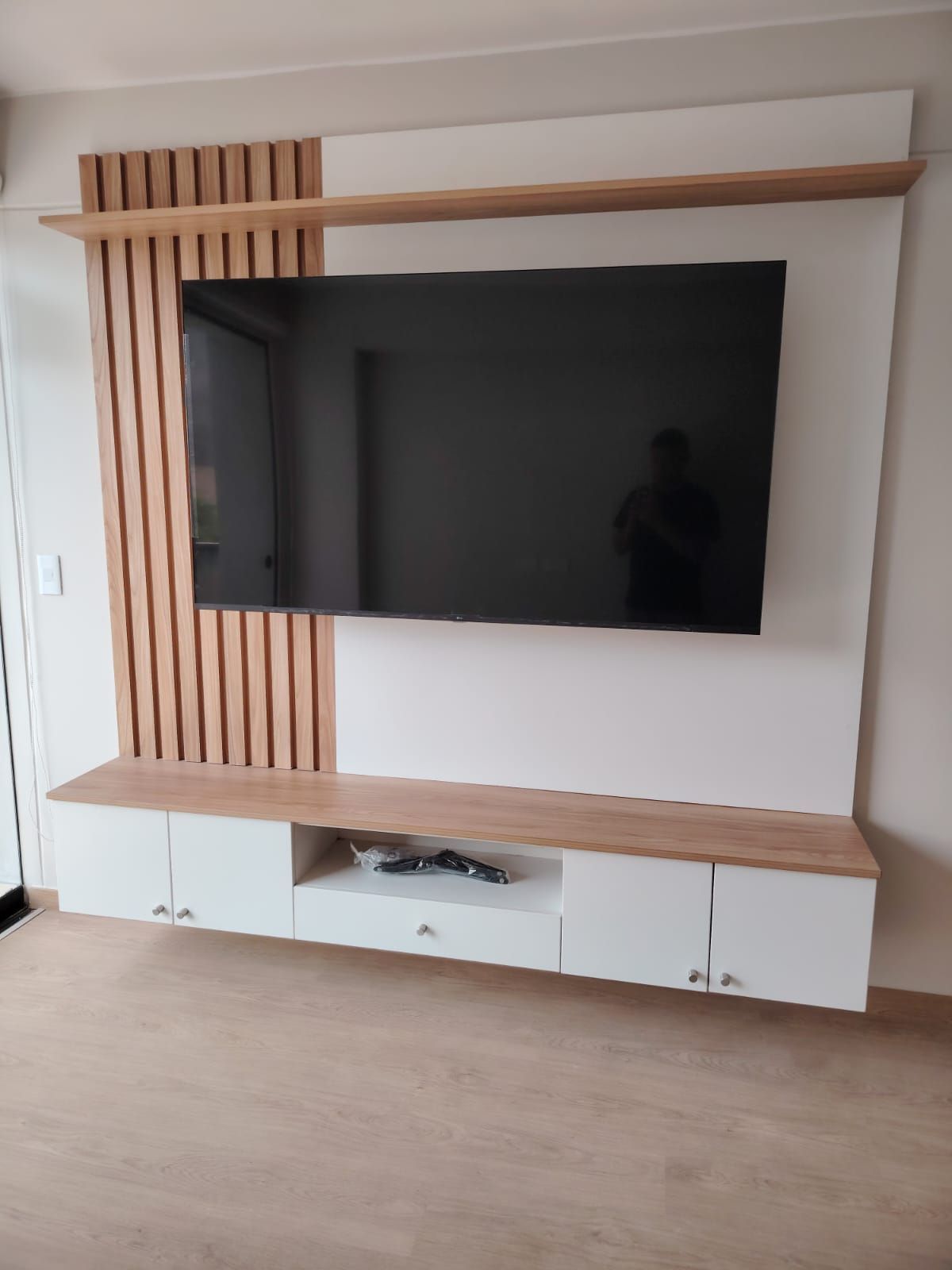 Mueble de TV moderno en color blanco y madera con televisión montada y muebles de almacenaje.