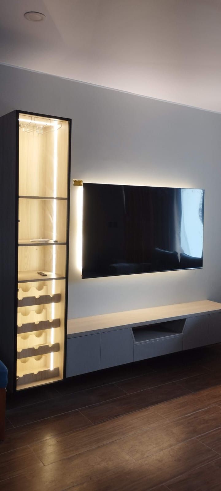 Sala de estar moderna con mueble para vinos iluminado, TV y consola multimedia contra una pared gris claro.
