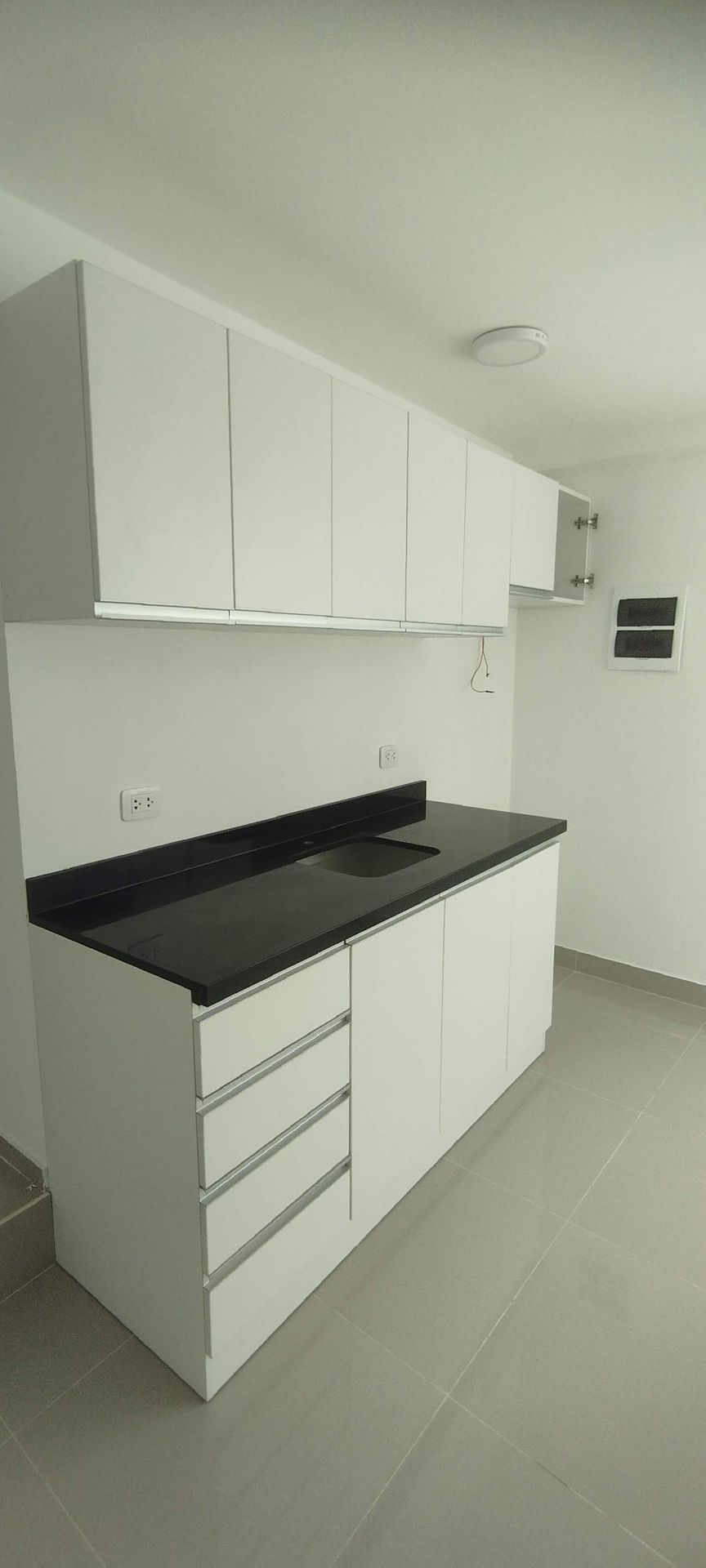 Gabinetes y cajones de cocina blancos con encimera negra.