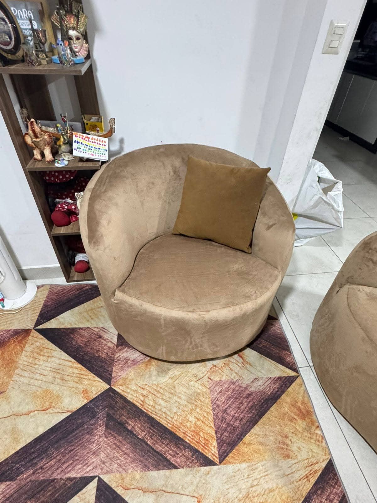 Sillón redondo de color tostado con almohada marrón sobre una alfombra estampada cerca de un estante.