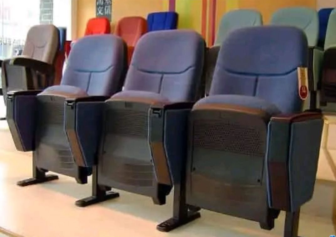 Filas de asientos de teatro azules con apoyabrazos y base negros, en un entorno interior.