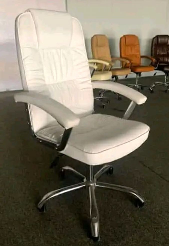 Silla de oficina de cuero blanco con base cromada. Otras sillas de color al fondo.
