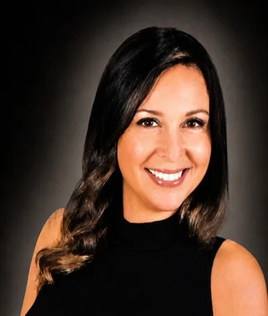 Smiling woman with shoulder-length brown hair in a blue top against a gray background