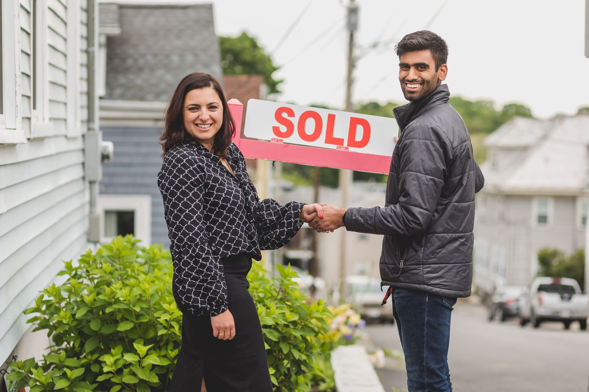 Real estate agent greeting a smiling couple outside a house with a 