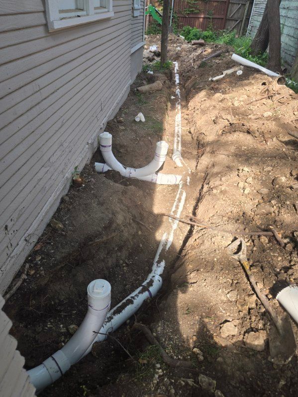 Gloved hand cleaning a sink drain under gray plumbing pipes in a bathroom or utility area