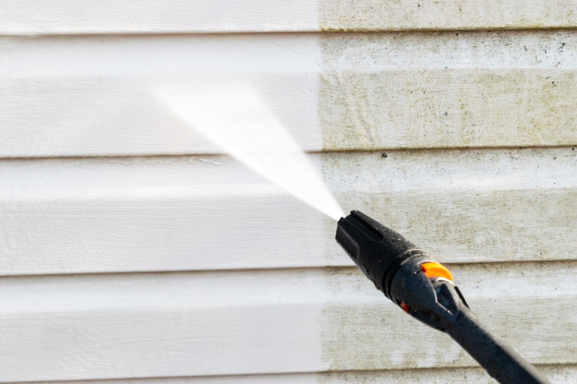 Pressure washer spraying a white house siding wall, removing dirt and grime