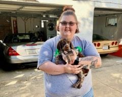 Woman holding a brown and white dog in front of a garage with cars.