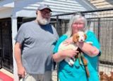 Couple holding a small dog at an outdoor shelter.