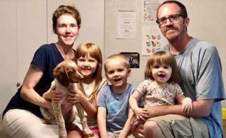 Family of five and dog smiling; seated together indoors.