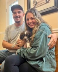 Couple holding a small, spotted puppy indoors, smiling.