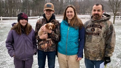 Family poses outside in winter, snow on the ground, holding a puppy.
