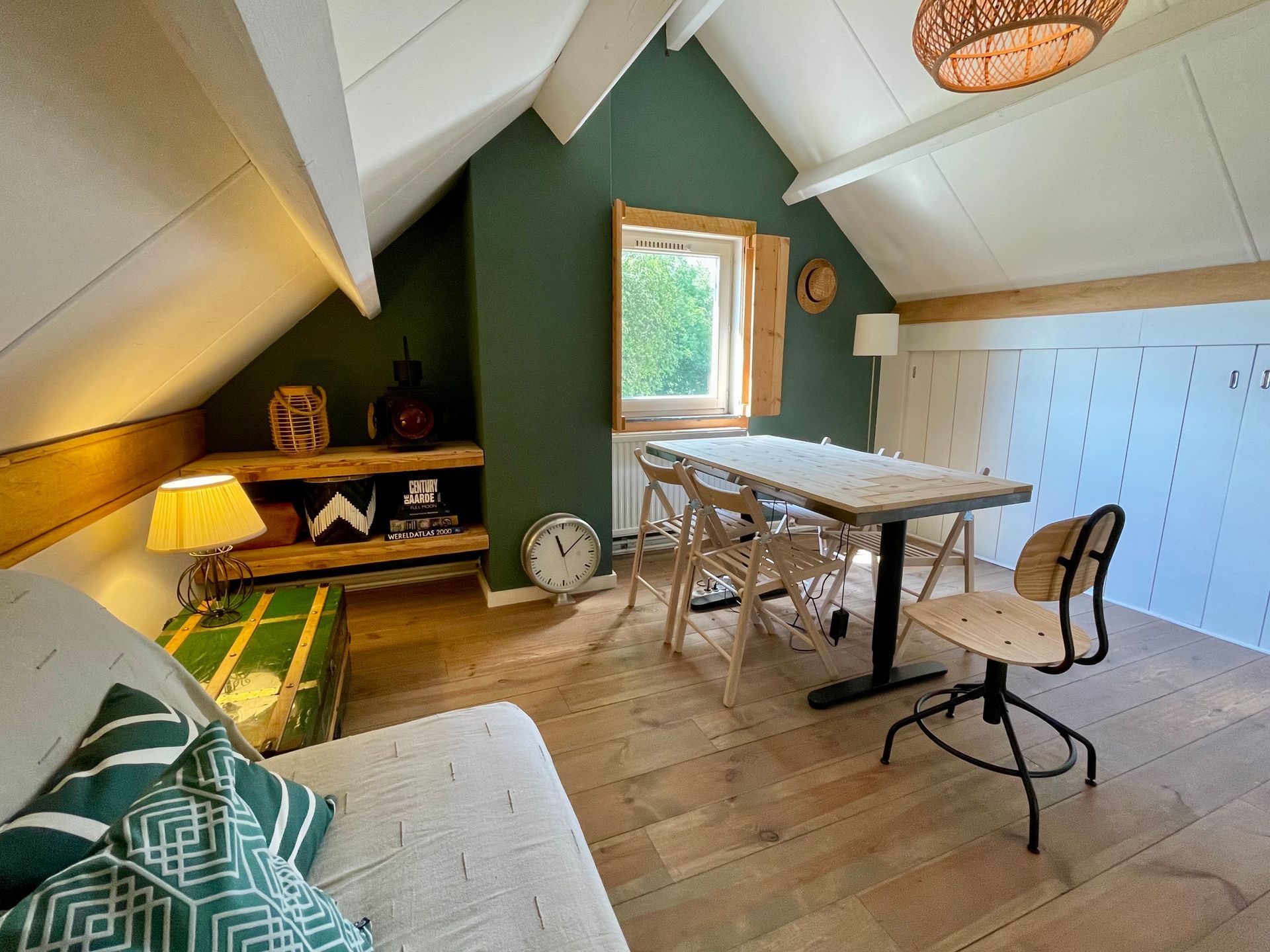 Attic room with wooden floors, green walls, dining table, and cozy seating.