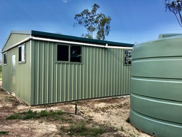 A Green Building With A Green Water Tank In Front Of It — Shed Constructions (QLD) In Gin Gin, QLD