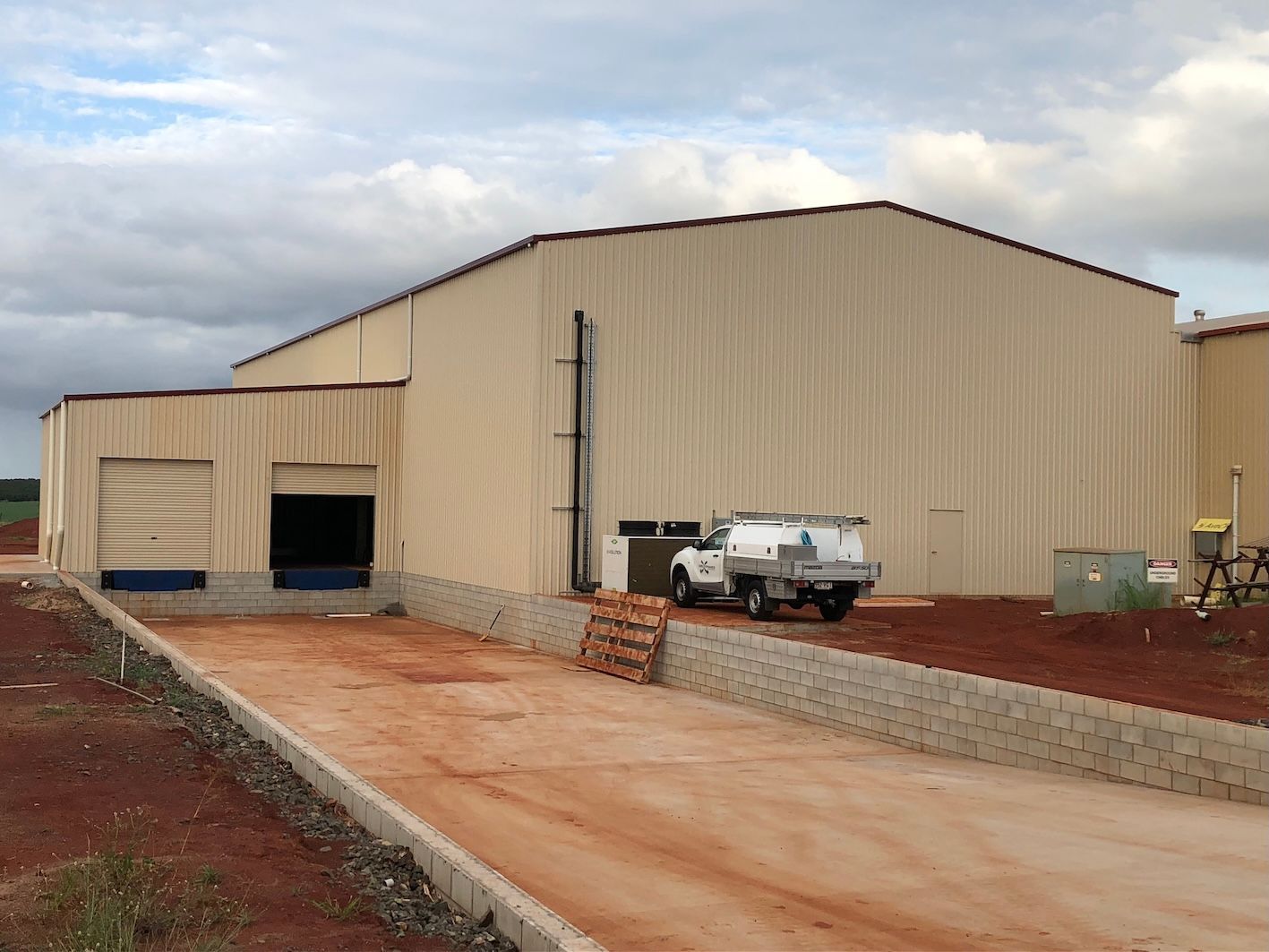 A large, beige industrial building with a loading dock and work truck parked outside.