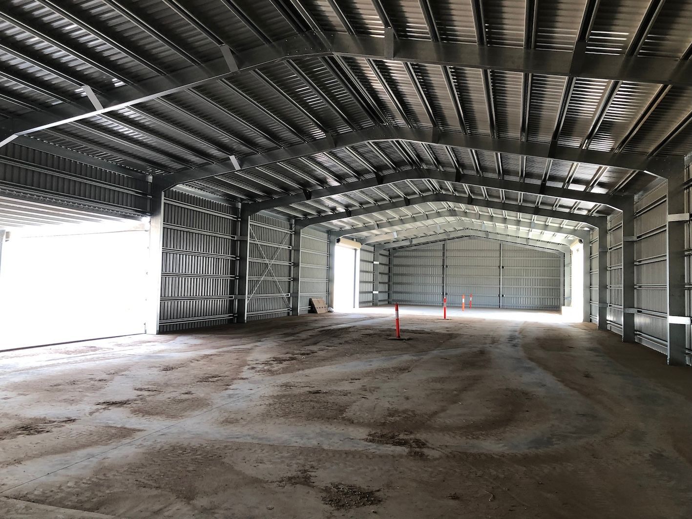 Interior view of an empty metal warehouse, with large open bay doors and exposed steel frame.