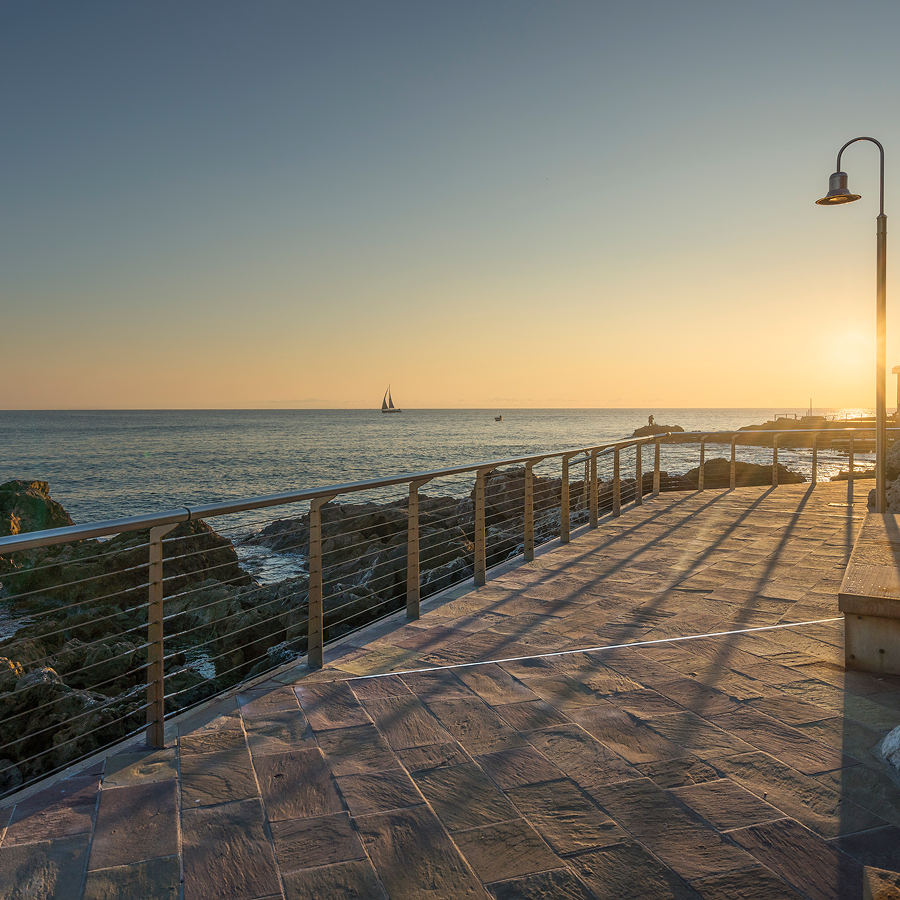 A pier with a fence leading to the ocean at sunset
