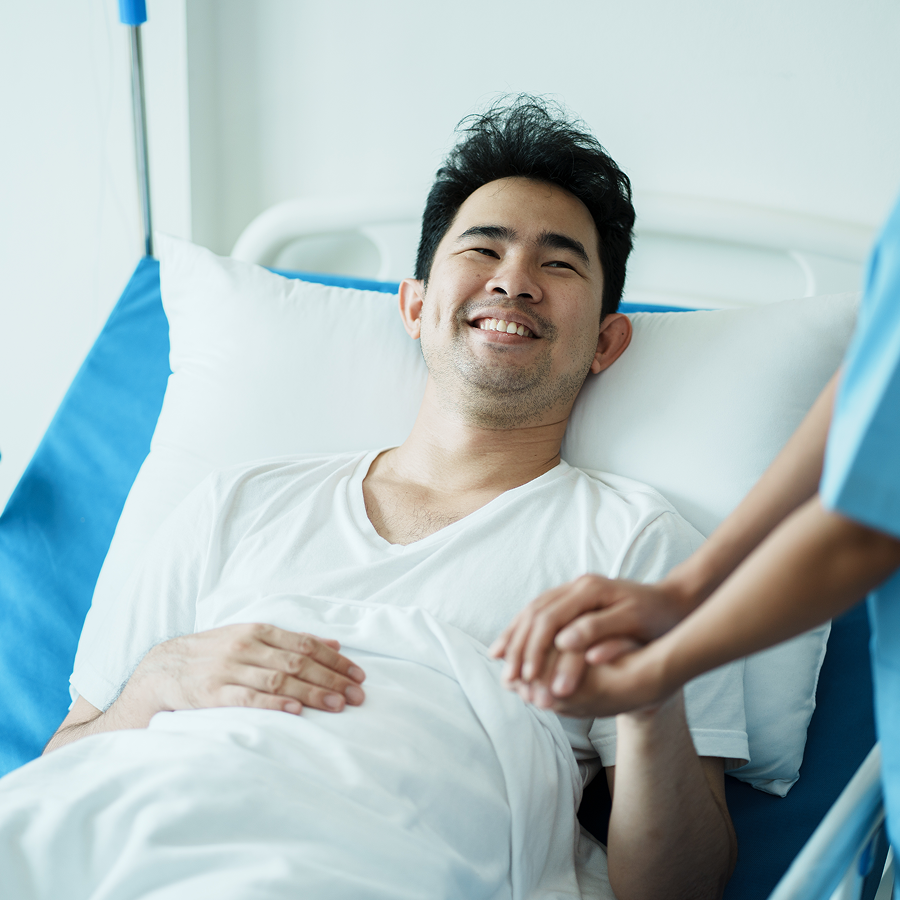 A man is laying in a hospital bed with a nurse holding his hand.
