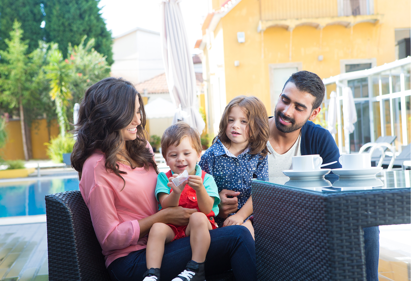 A family is sitting at a table in front of a swimming pool.