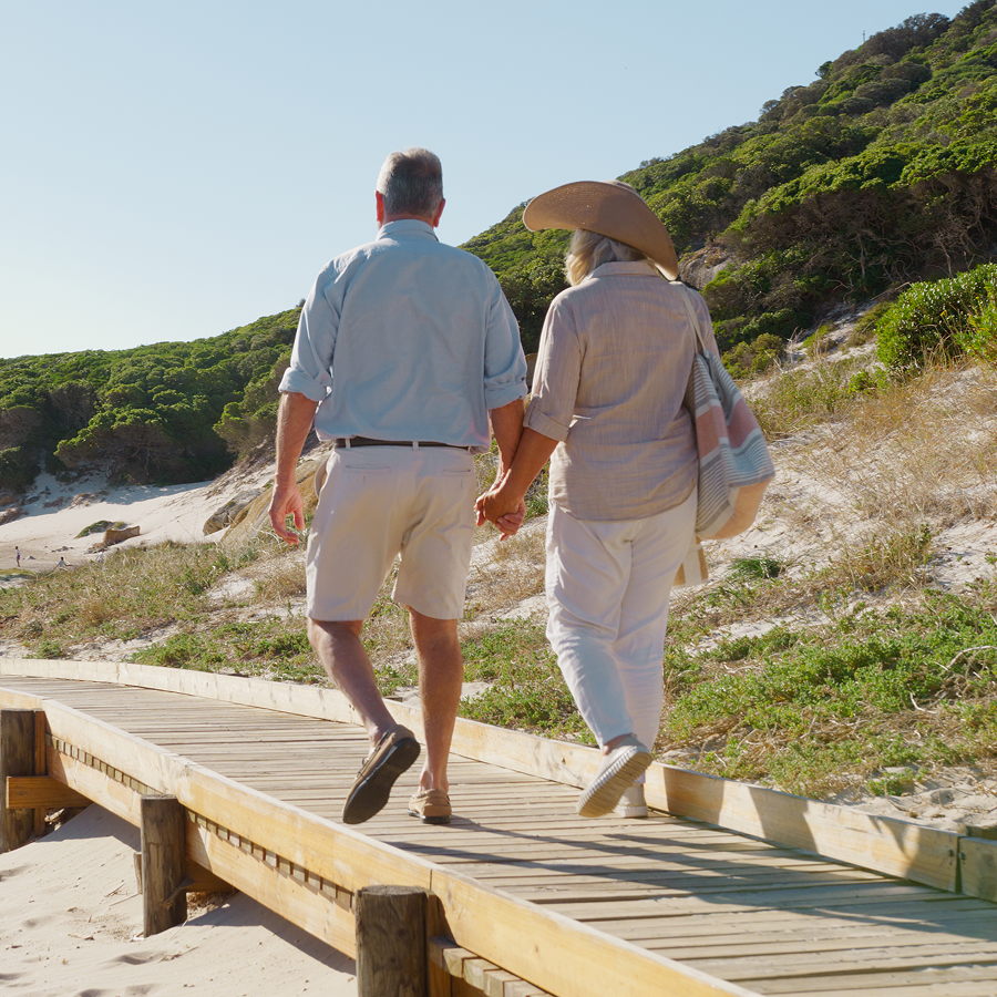 A man and woman are walking on a wooden boardwalk holding hands.