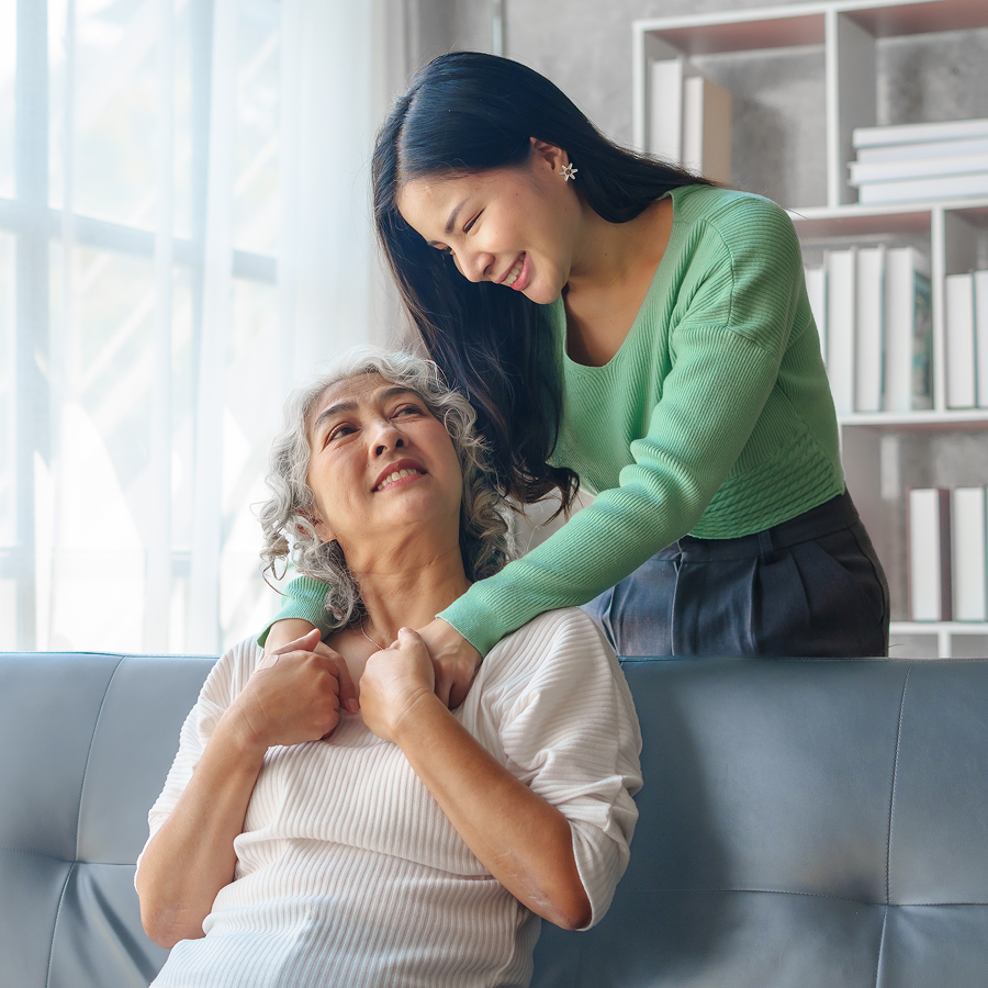 A woman is putting her hand on an older woman 's neck while sitting on a couch.