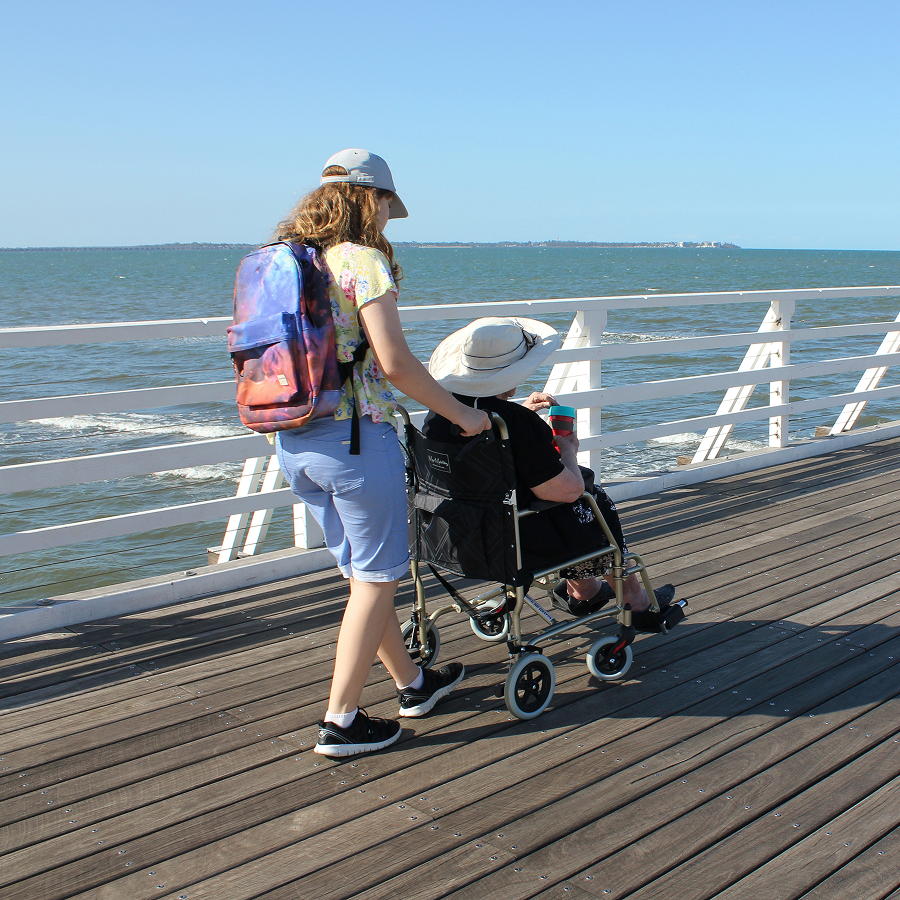 A woman pushes a child in a wheelchair on a pier