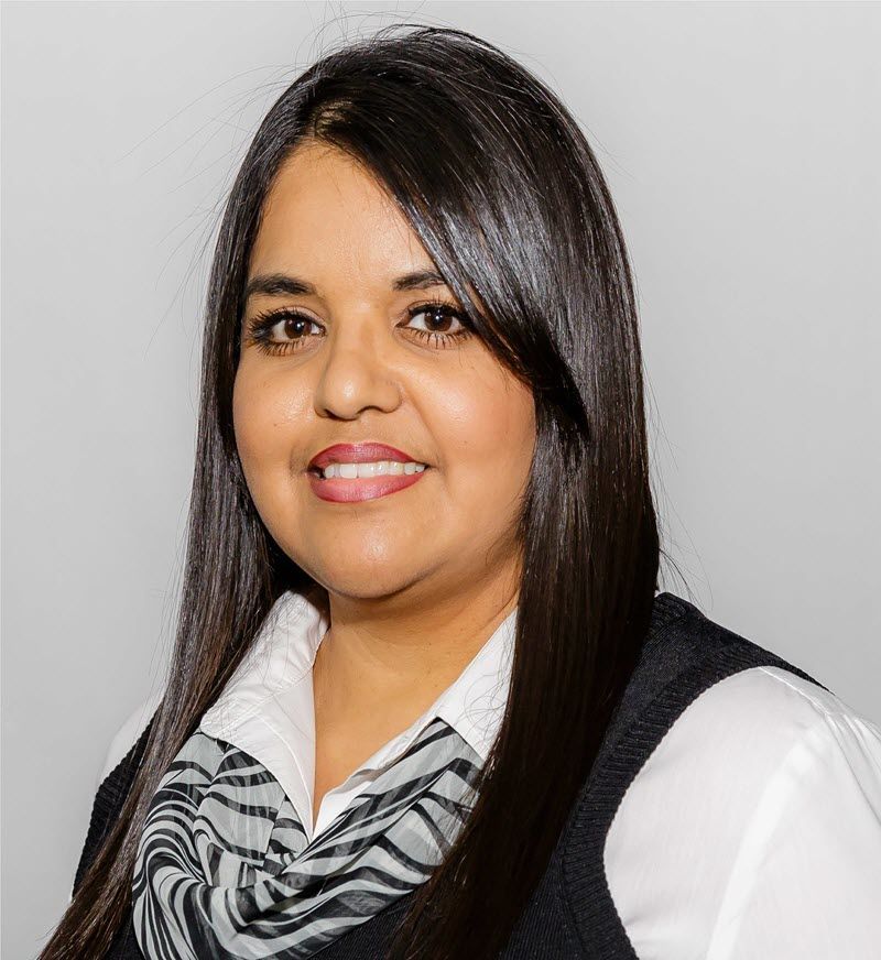 Woman in black suit smiles at the camera against a grey backdrop.