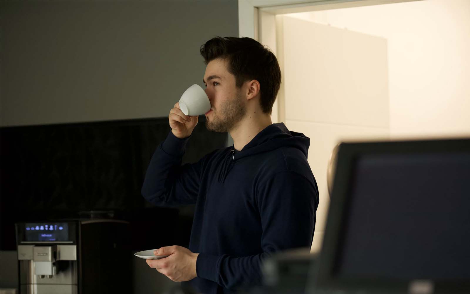 A man is drinking a cup of coffee in a dark room.
