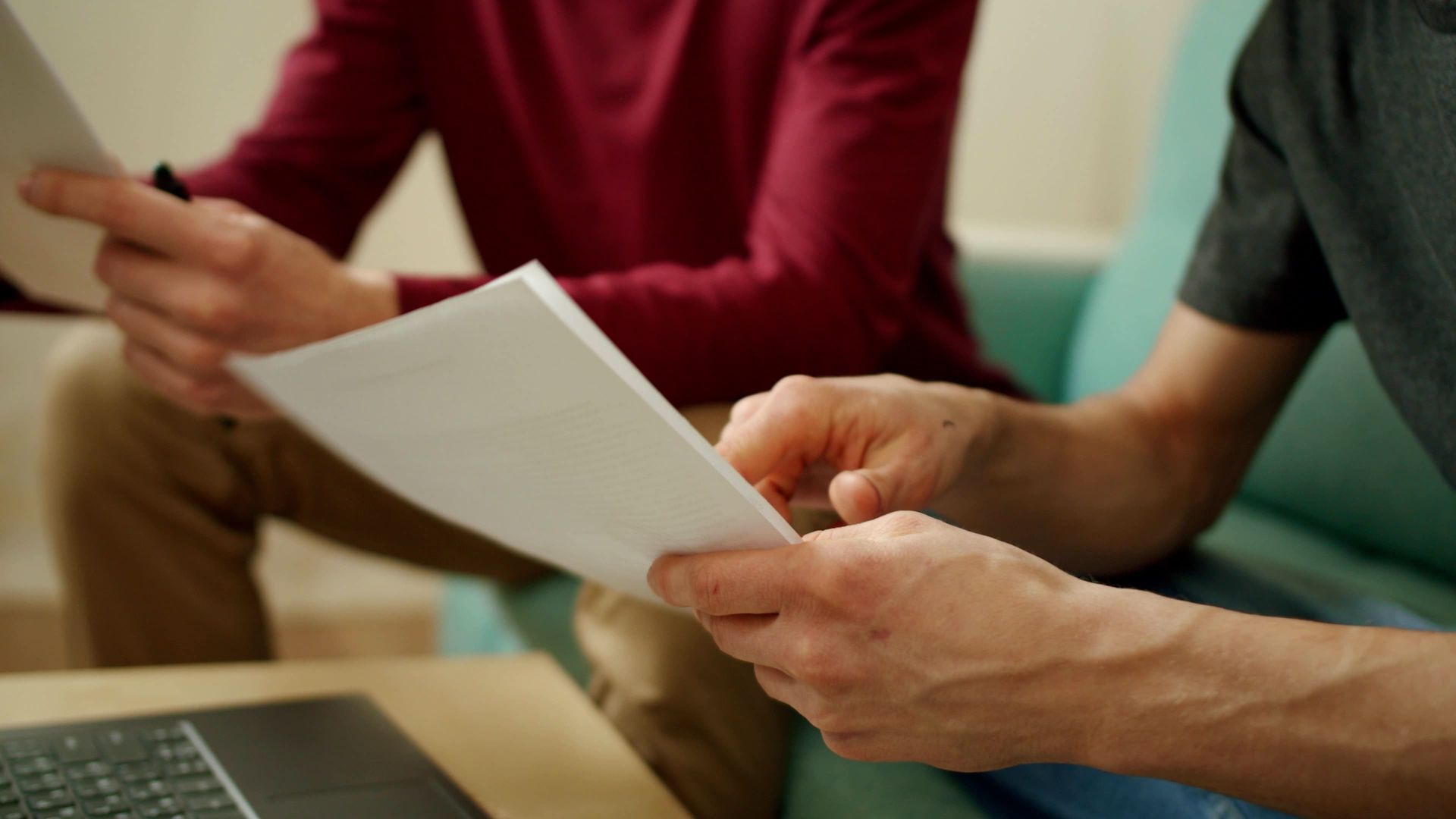 Two men are sitting on a couch looking at a piece of paper.