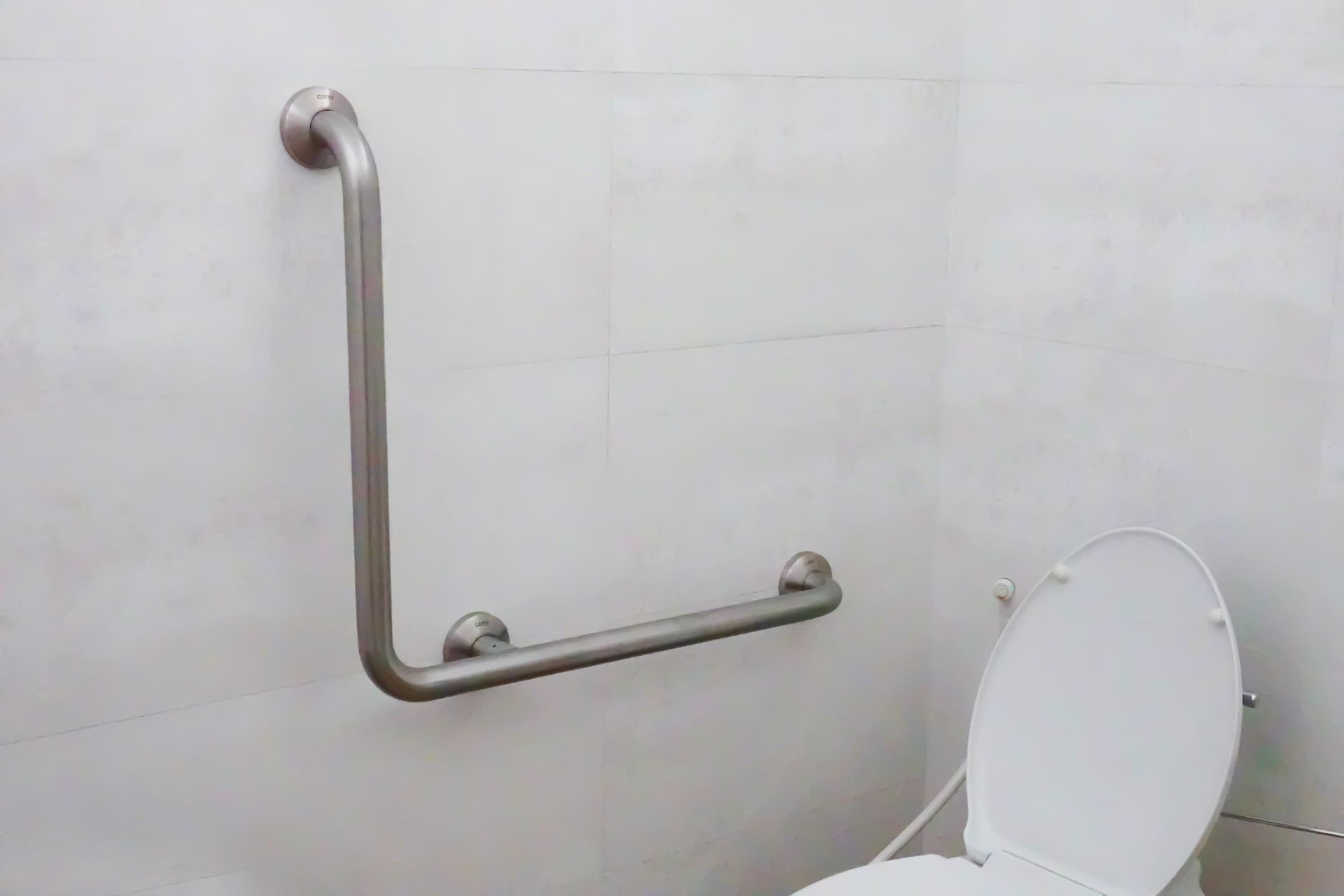 A bathroom with a toilet and a hand rail on the wall.
