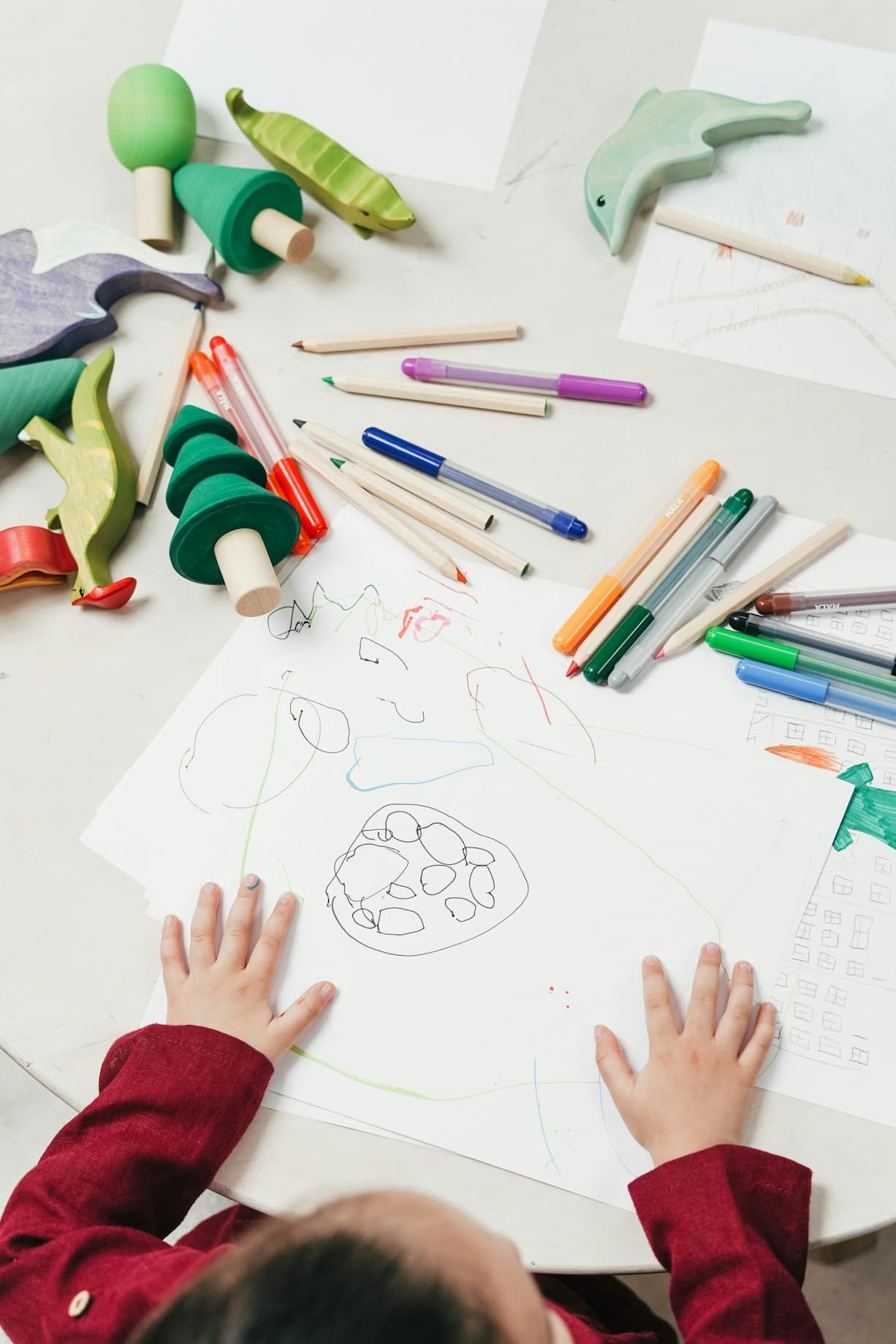 A child is sitting at a table drawing with markers and pencils.