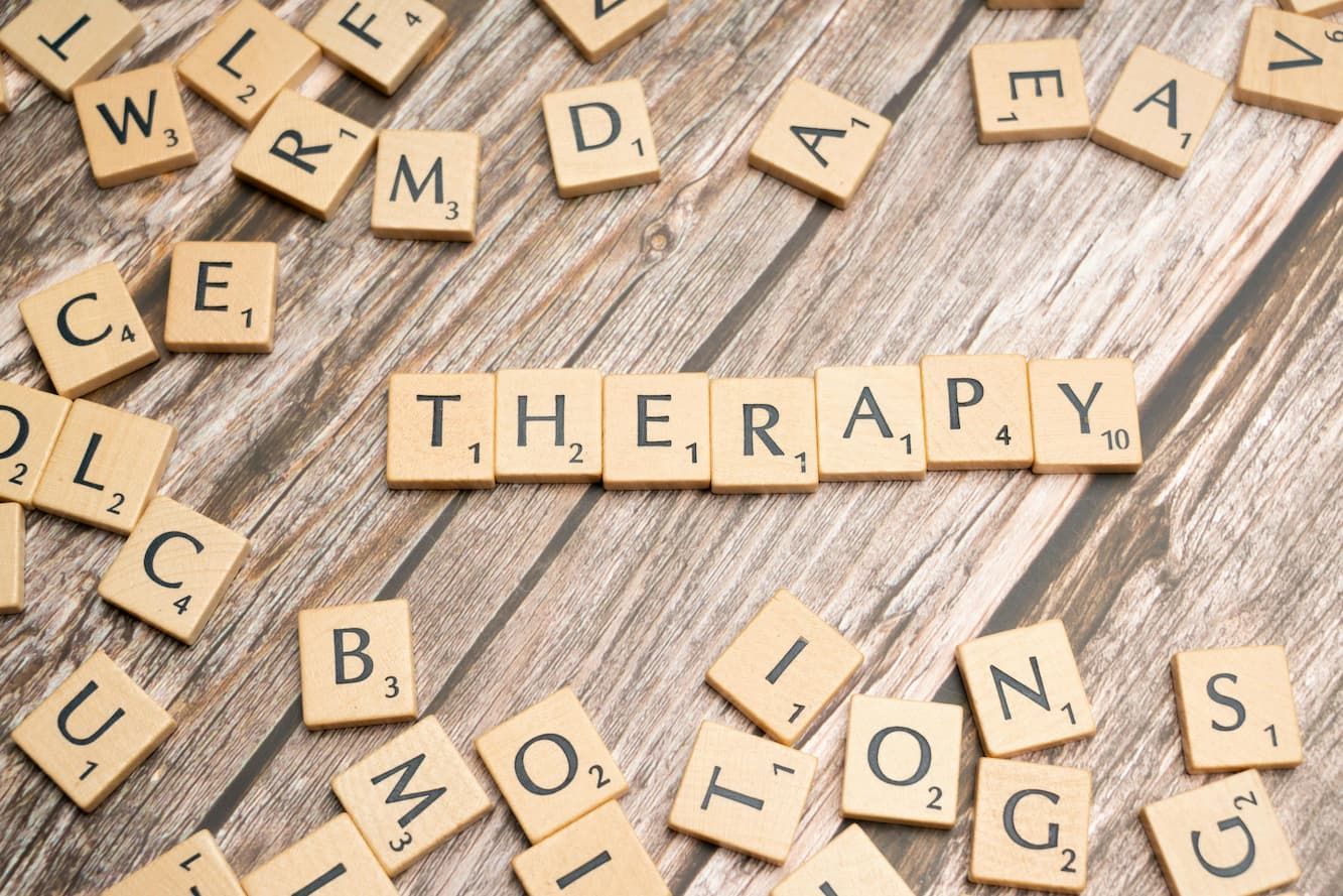 The word therapy is written in scrabble tiles on a wooden table