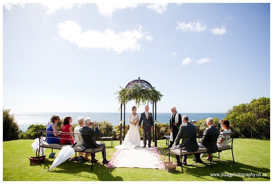 A bride and groom are getting married under a gazebo in front of the ocean.