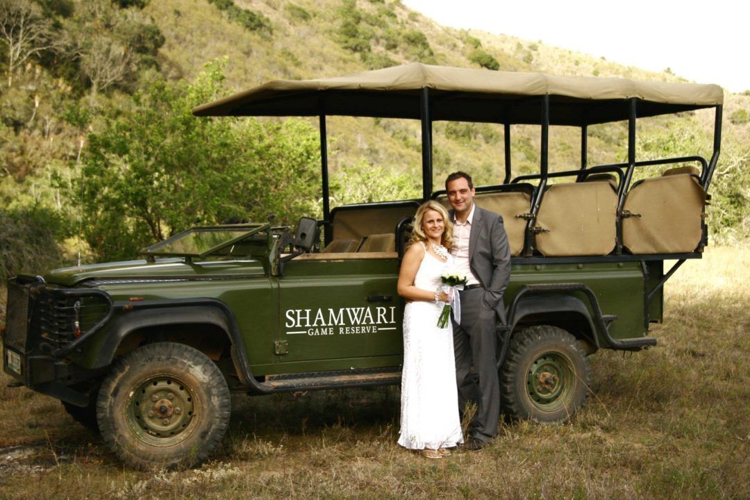 A bride and groom are posing for a picture in front of a safari vehicle.