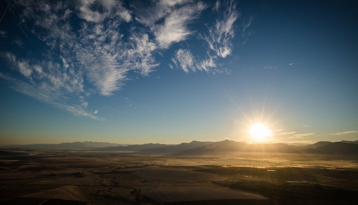The sun is setting over a desert landscape with mountains in the background.