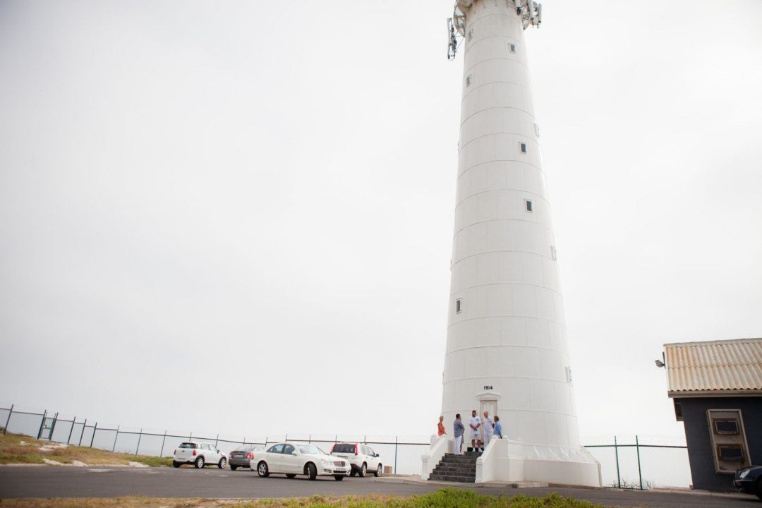 A white lighthouse with cars parked in front of it.