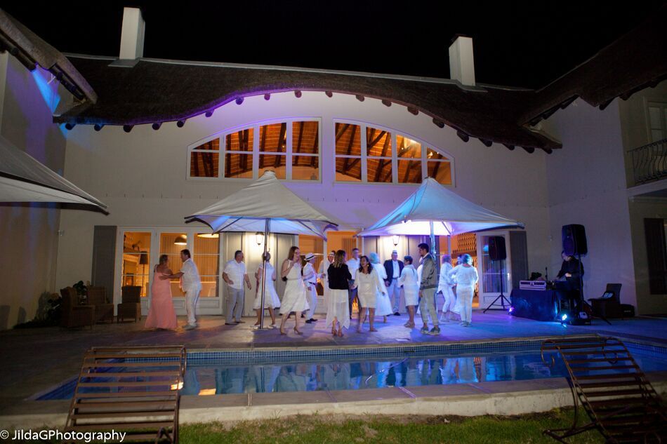 A group of people are dancing in front of a house with a swimming pool.