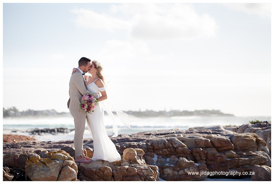 A bride and groom are kissing on a rocky beach.