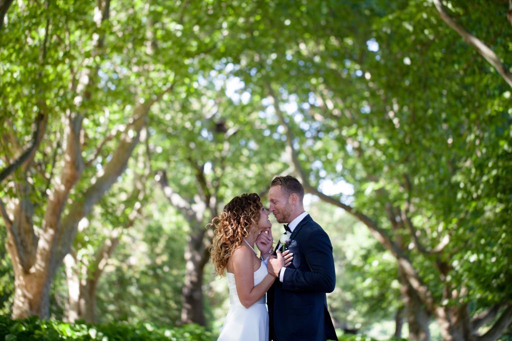 A bride and groom are dancing in a park surrounded by trees.