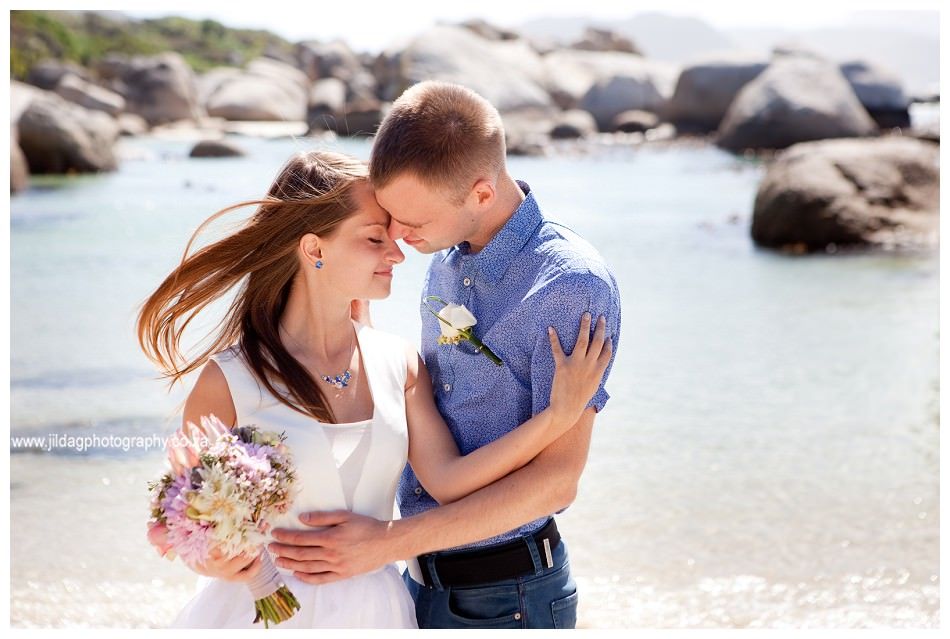 A bride and groom are posing for a picture on the beach.